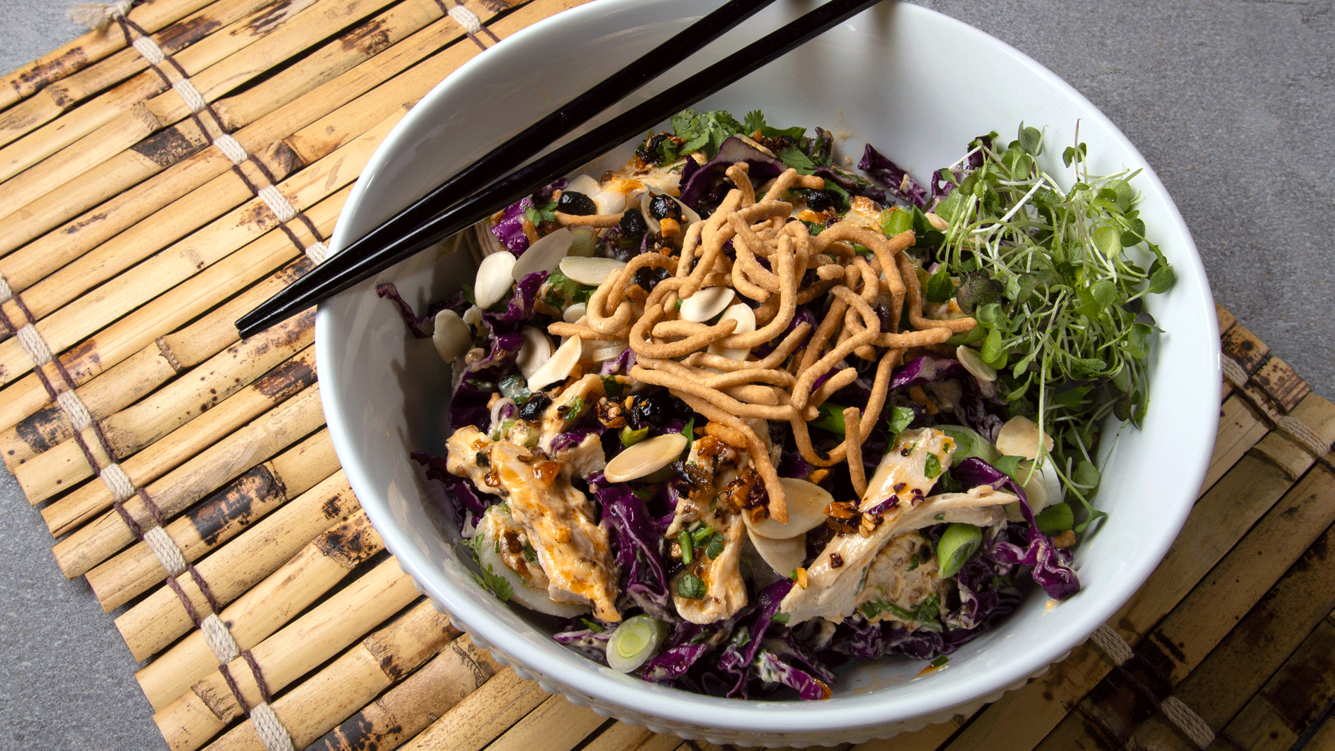 White bowl with Chinese chicken salad, topped with chow mein noodles on bamboo mat with chopsticks #myoomame