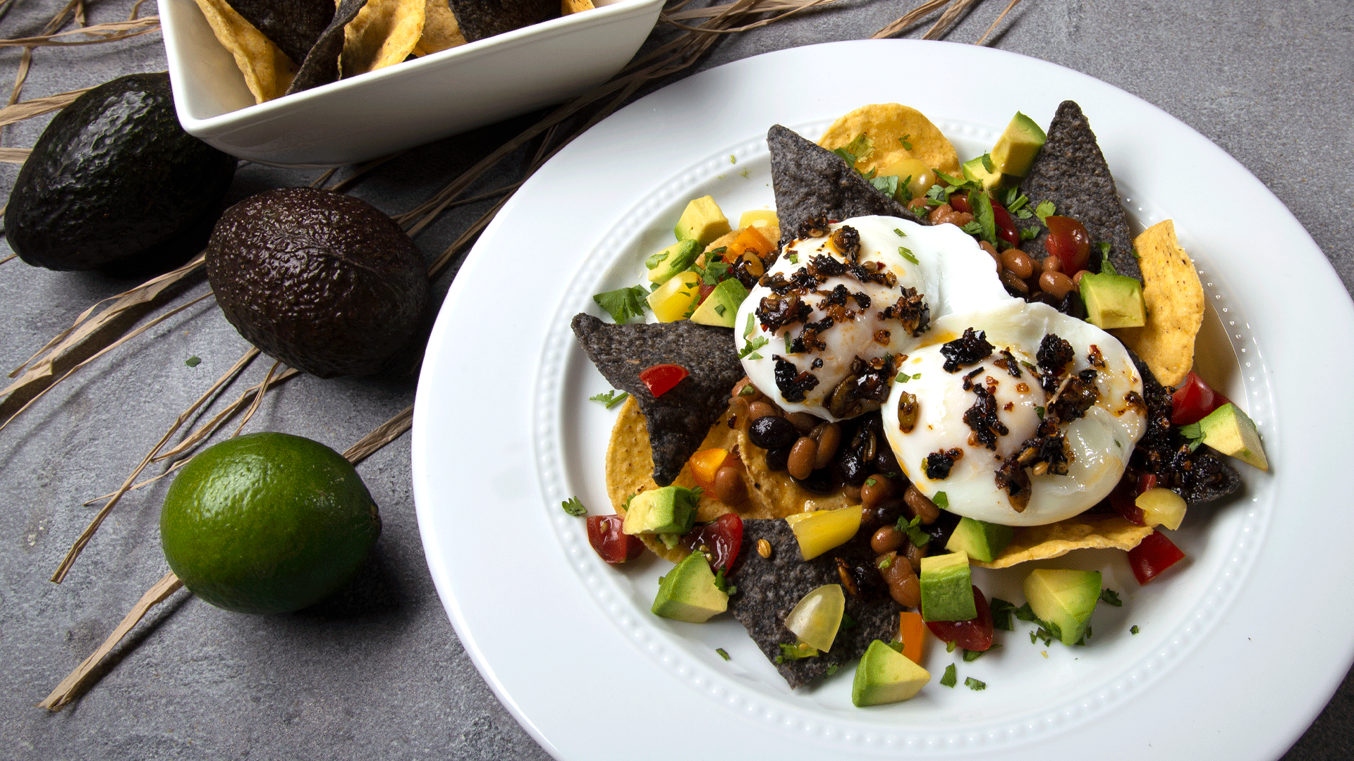 White round plate with chips, poached eggs, topped with Mexican oo’mämē Chile Infusion, avocado and tomatoes #huevos #myoomame