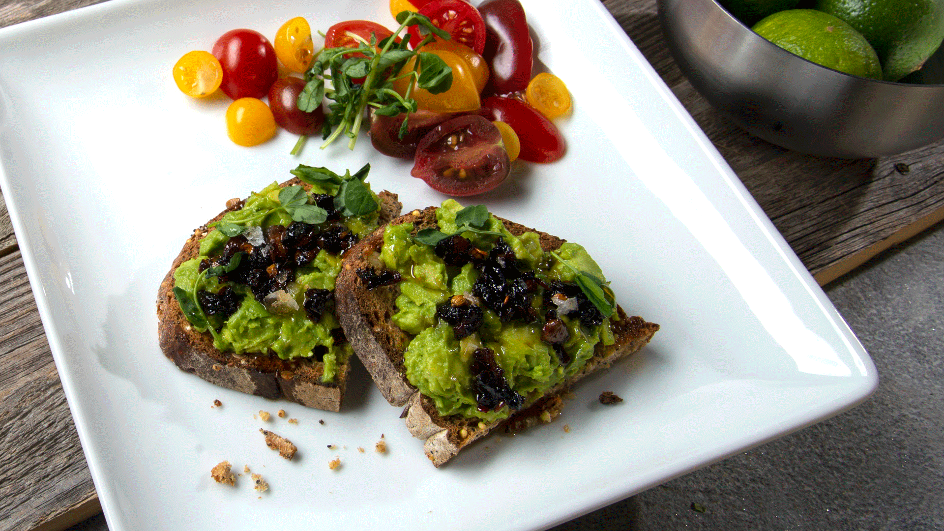 Square white plate with avocado toast topped with oo’mämē Chile Infusion and heirloom cherry tomatoes #avocadotoast