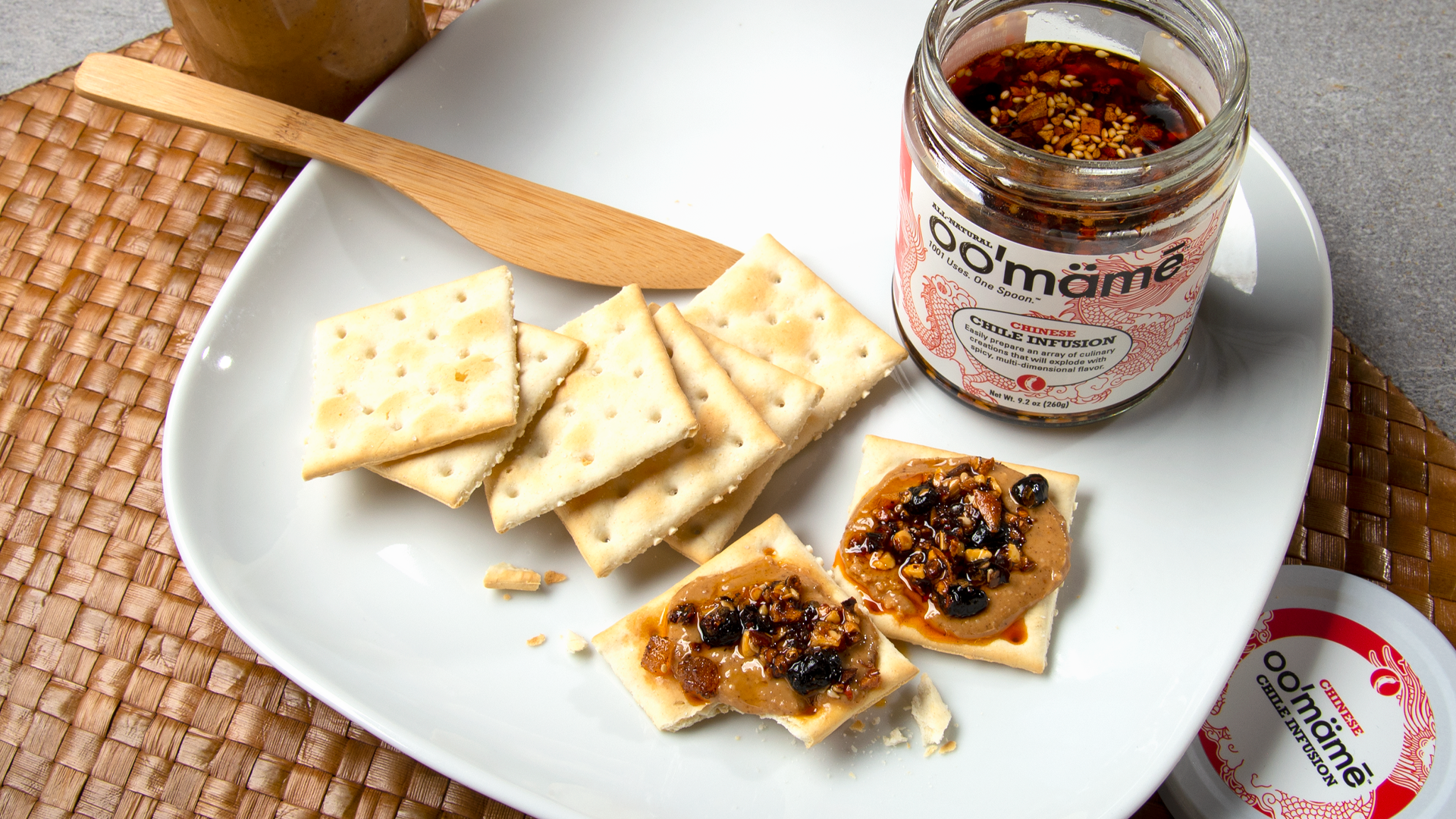 White plate on woven mat with a jar of Chinese oo’mämē chile infusion, saltines topped with peanut butter and oo’mämē #myoomame