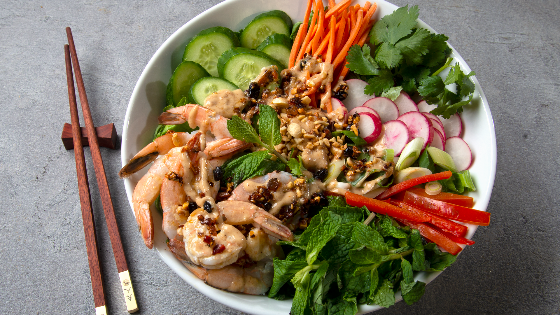 White shallow bowl with Chinese shrimp salad: Cucumbers, radishes, carrots, peppers, shrimp and herbs, topped with oo’mämē Chinese dressing #spicydressing #myoomame