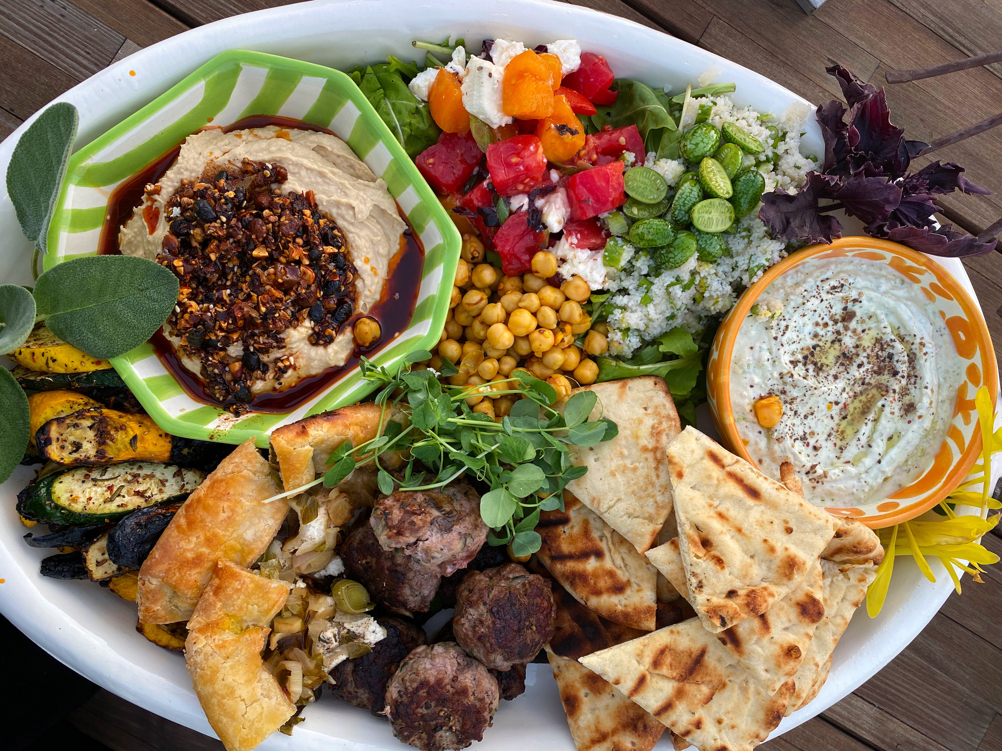 Mezze platter with grilled vegetables, lamb sliders, hummus, tomato and sheep cheese, fonio, yogurt dip and pita