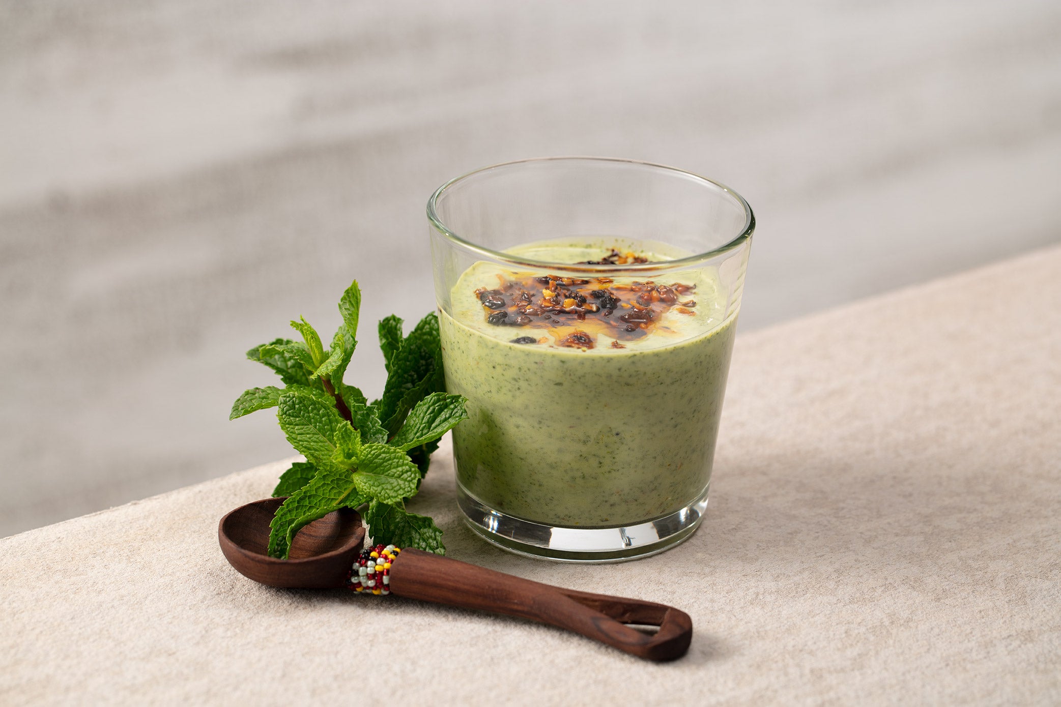 Double old fashioned glass with creamy mint dressing, wooden spoon and sprigs of mint on cream colored background