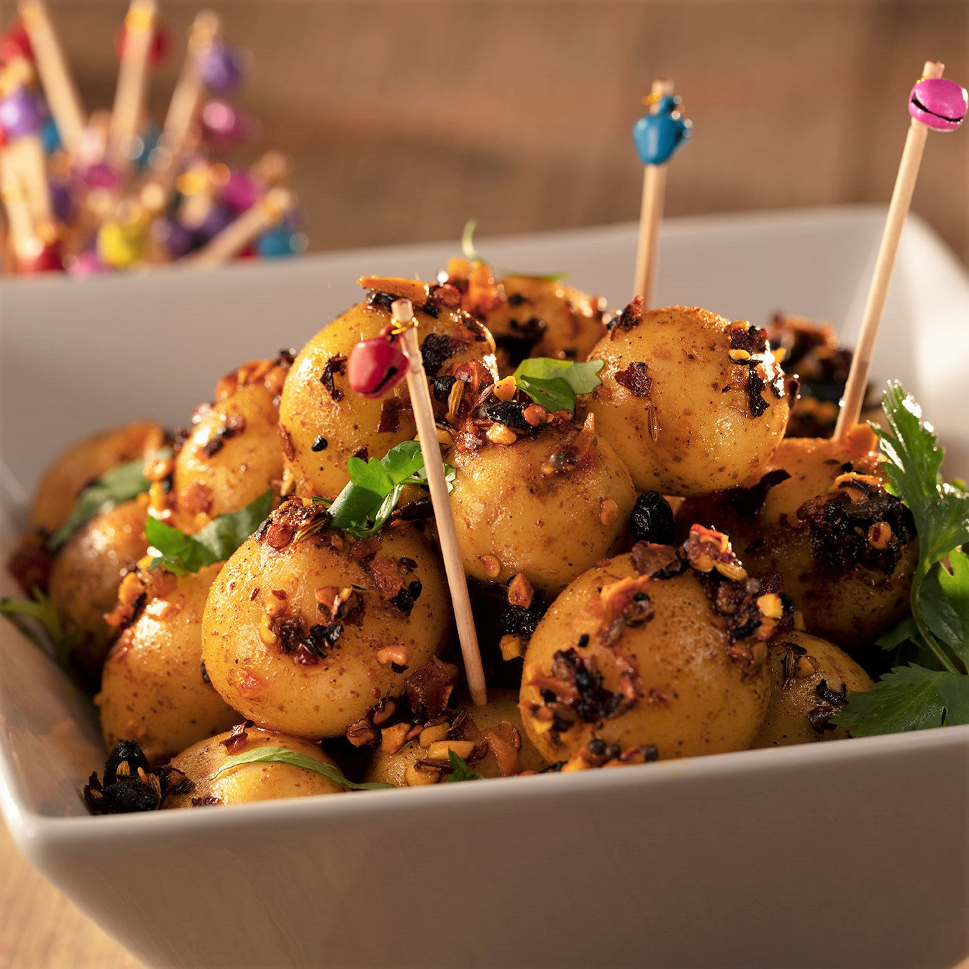 square white bowl with mini potatoes roasted with oo’mämē Chile Crisp, chopped cilantro and toothpicks with tiny colorful bells