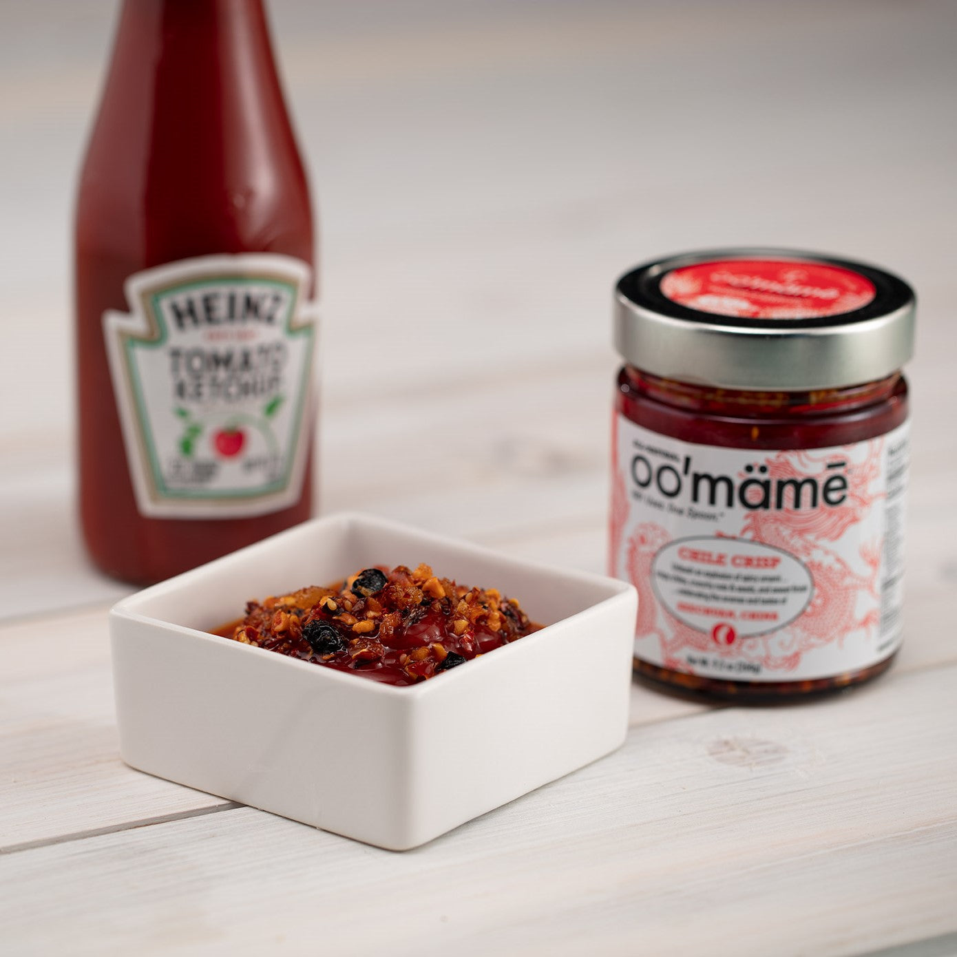 Square white dish with ketchup and oo’mämē, jar of oo’mämē Chinese Chile Crisp and bottle of ketchup