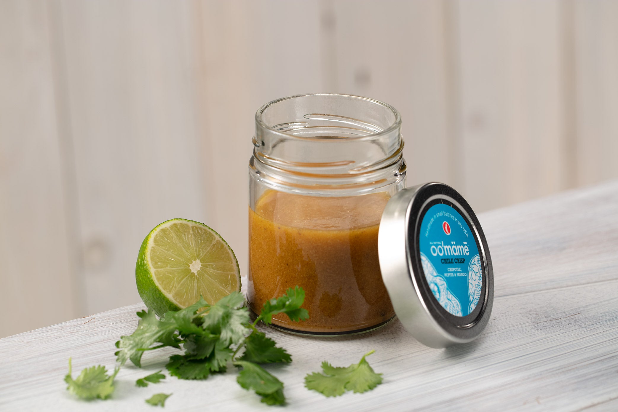 Jar of oo’mämē lemon vinaigrette with lime half and fresh cilantro