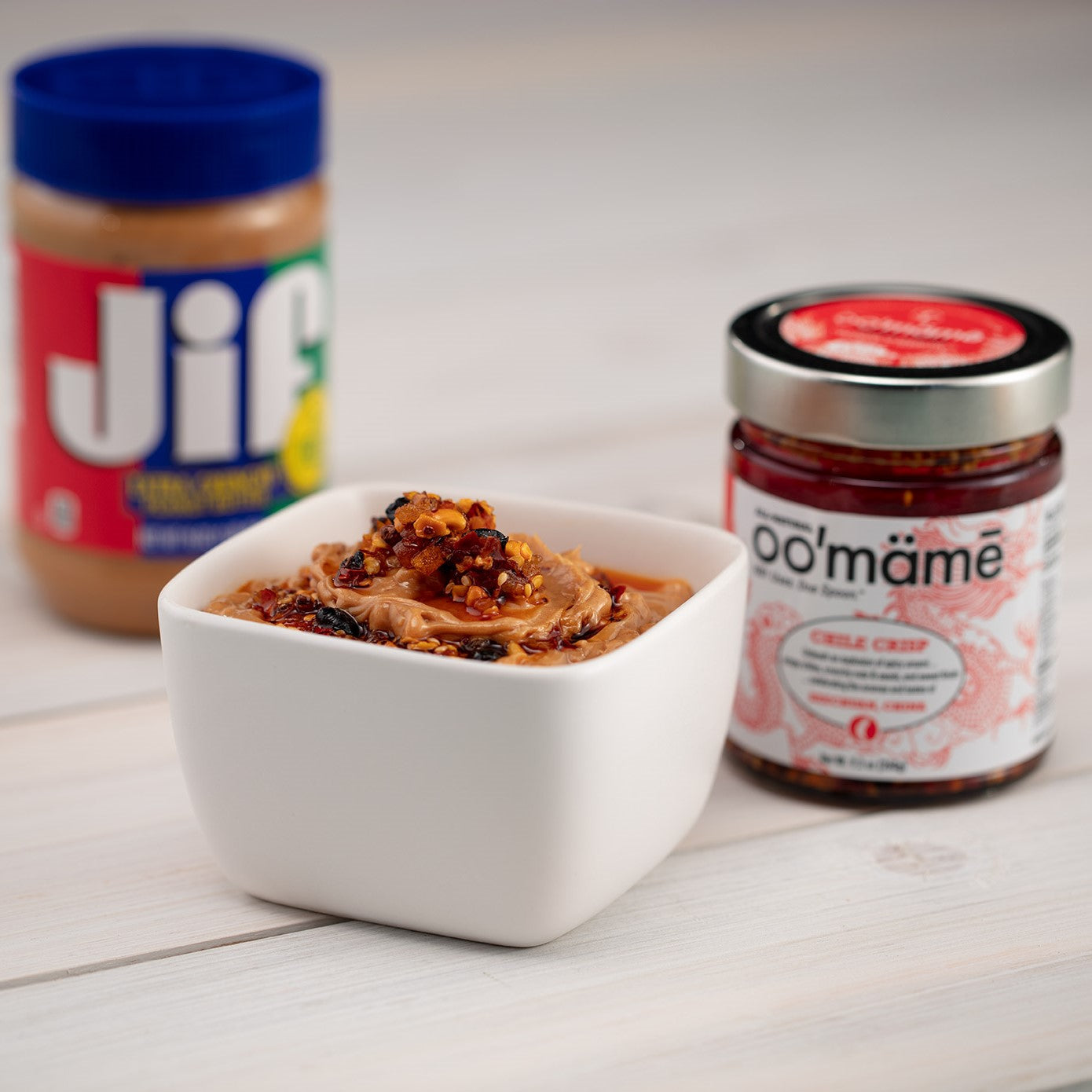 Square white bowl of peanut butter and oo’mämē, with a jar of Chinese oo’mämē and a jar of Jif peanut butter.