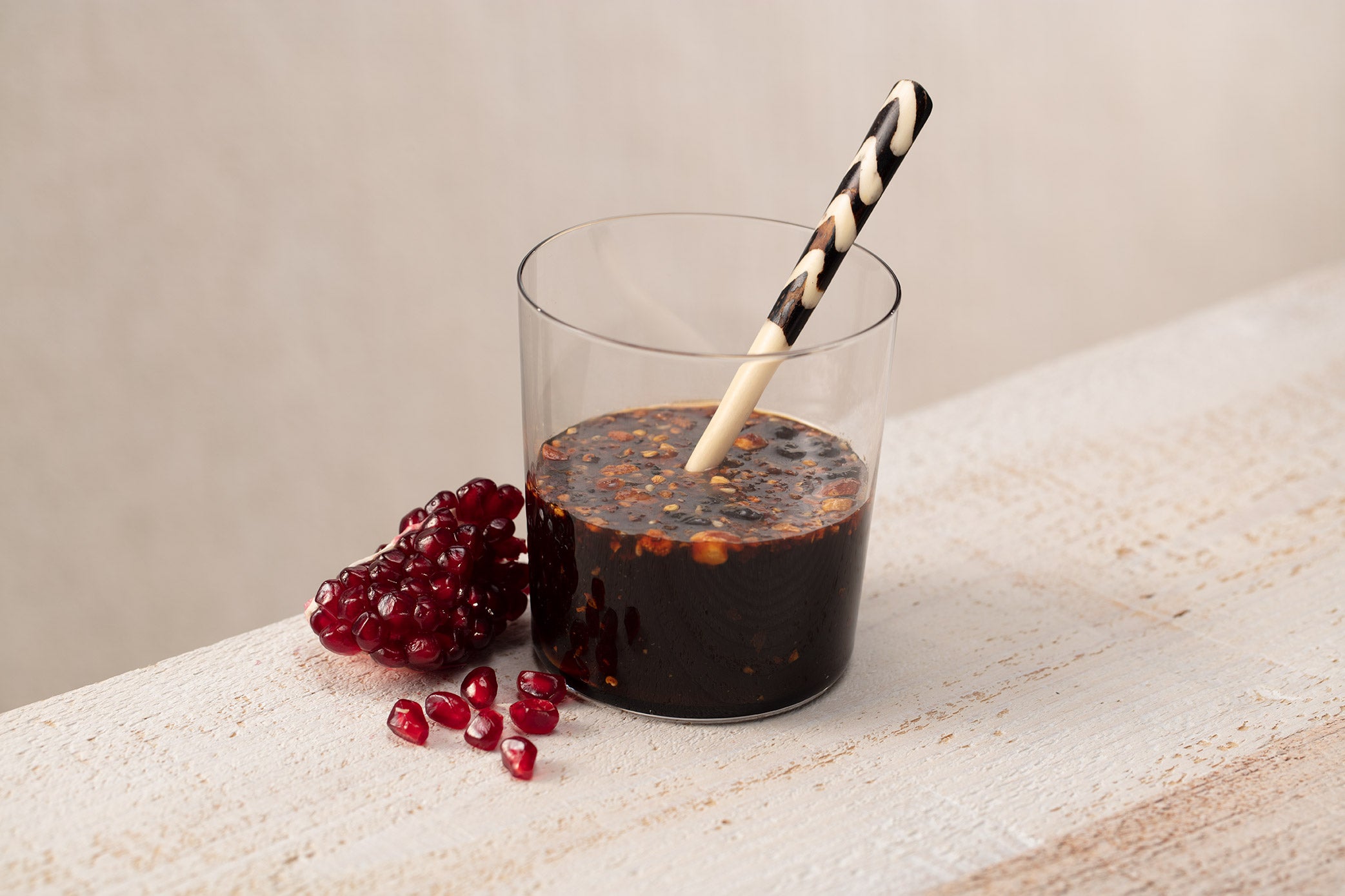 Glass with pomegranate molasses oo’mämē dressing, black and white spoon and pomegranate arils
