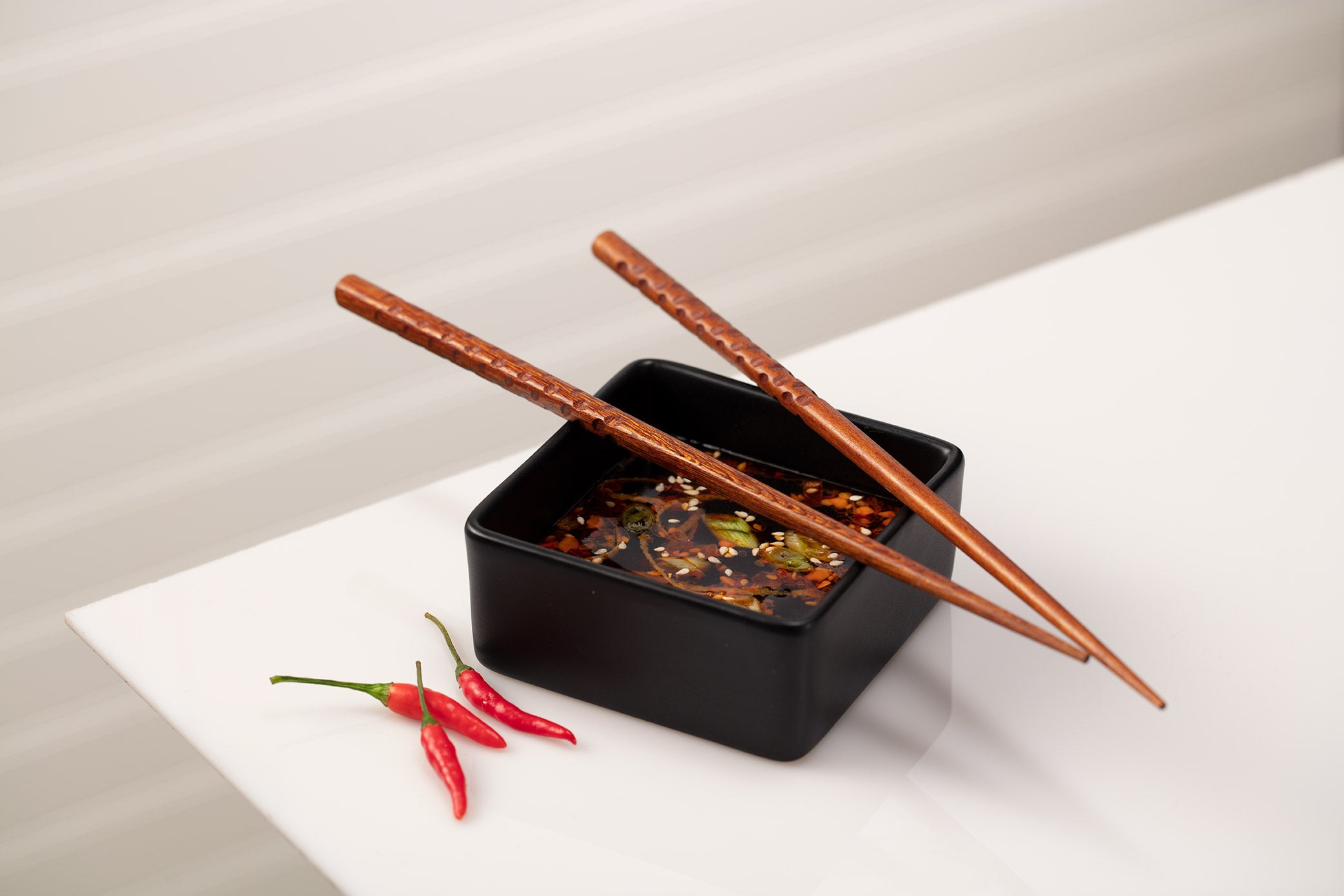 Square black dish with dumpling dipping sauce, chopsticks and red chile peppers