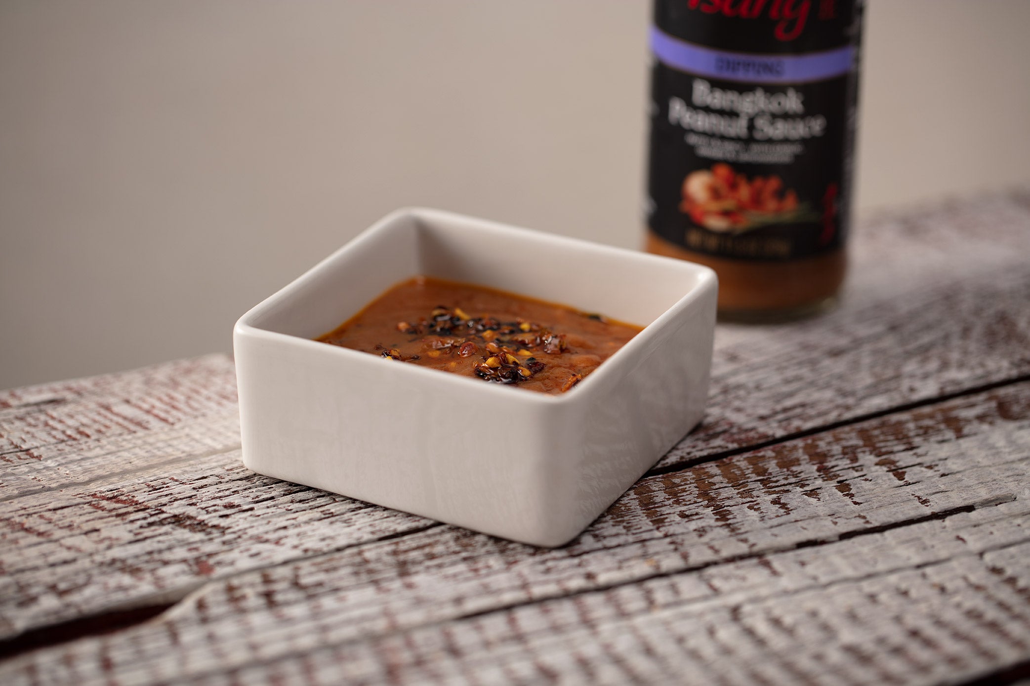 square white bowl with peanut sauce and a bottle of Bangkok Satay Sauce