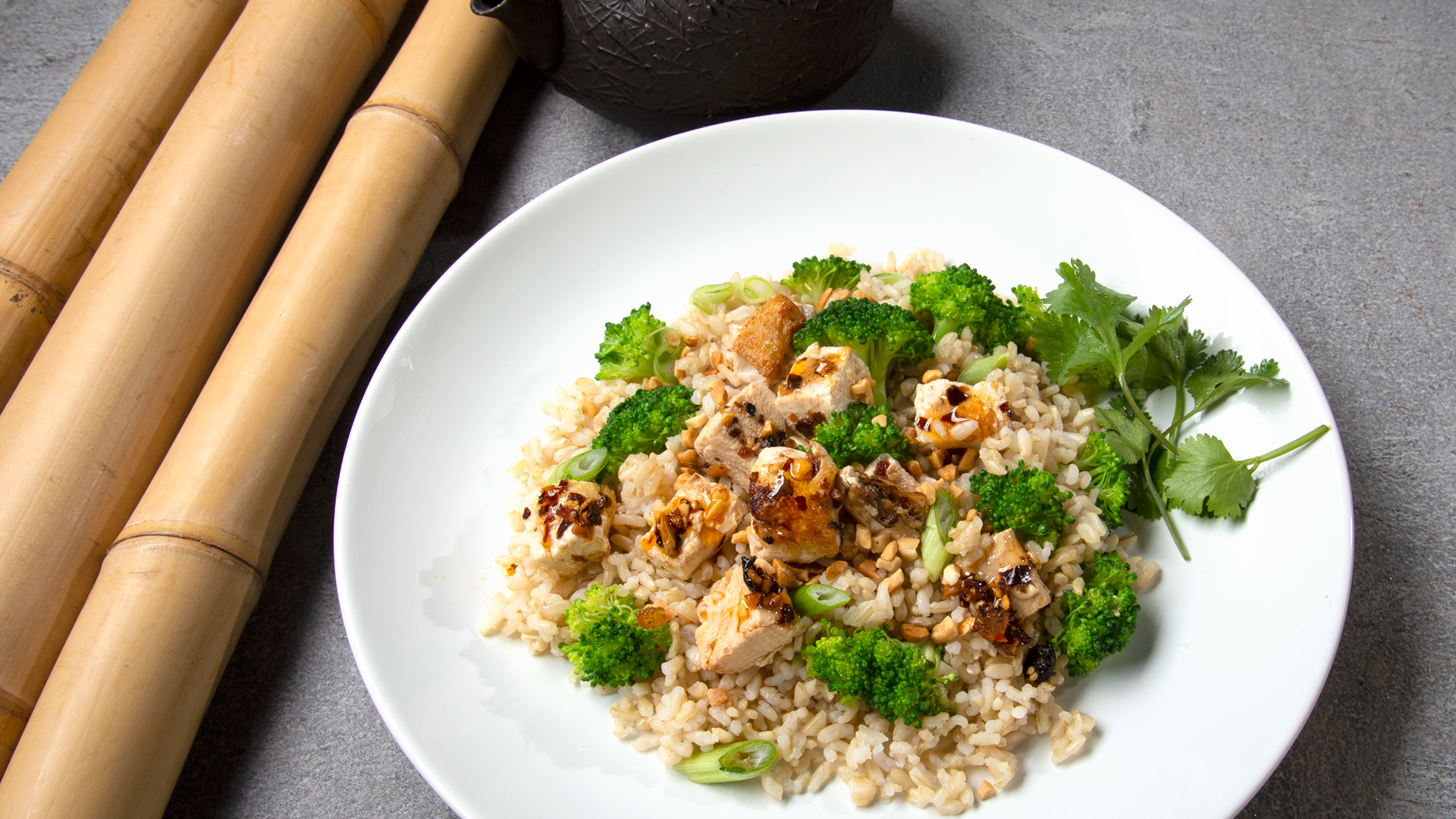 White plate with broccoli, tofu marinated in oo’mämē, and brown rice with cilantro. Bamboo reeds. #veganrecipe #myoomame