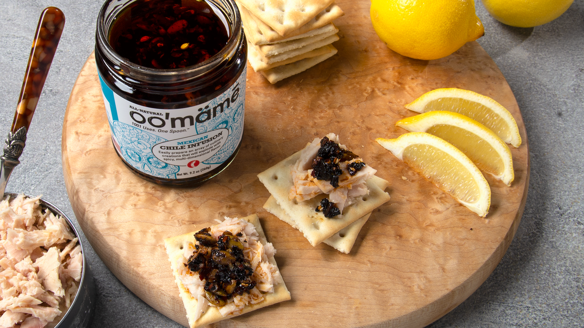 Round wooden board with oo’mämē Mexican Chile Infusion, saltines with tuna fish and lemon wedges. #tunahelper #myoomame