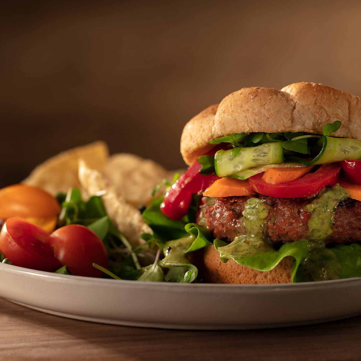 Veggie burger on a whole wheat bun with cilantro mint oo’mämē dressing, pickled vegetables, lettuce and tomato with a small salad and corn chips