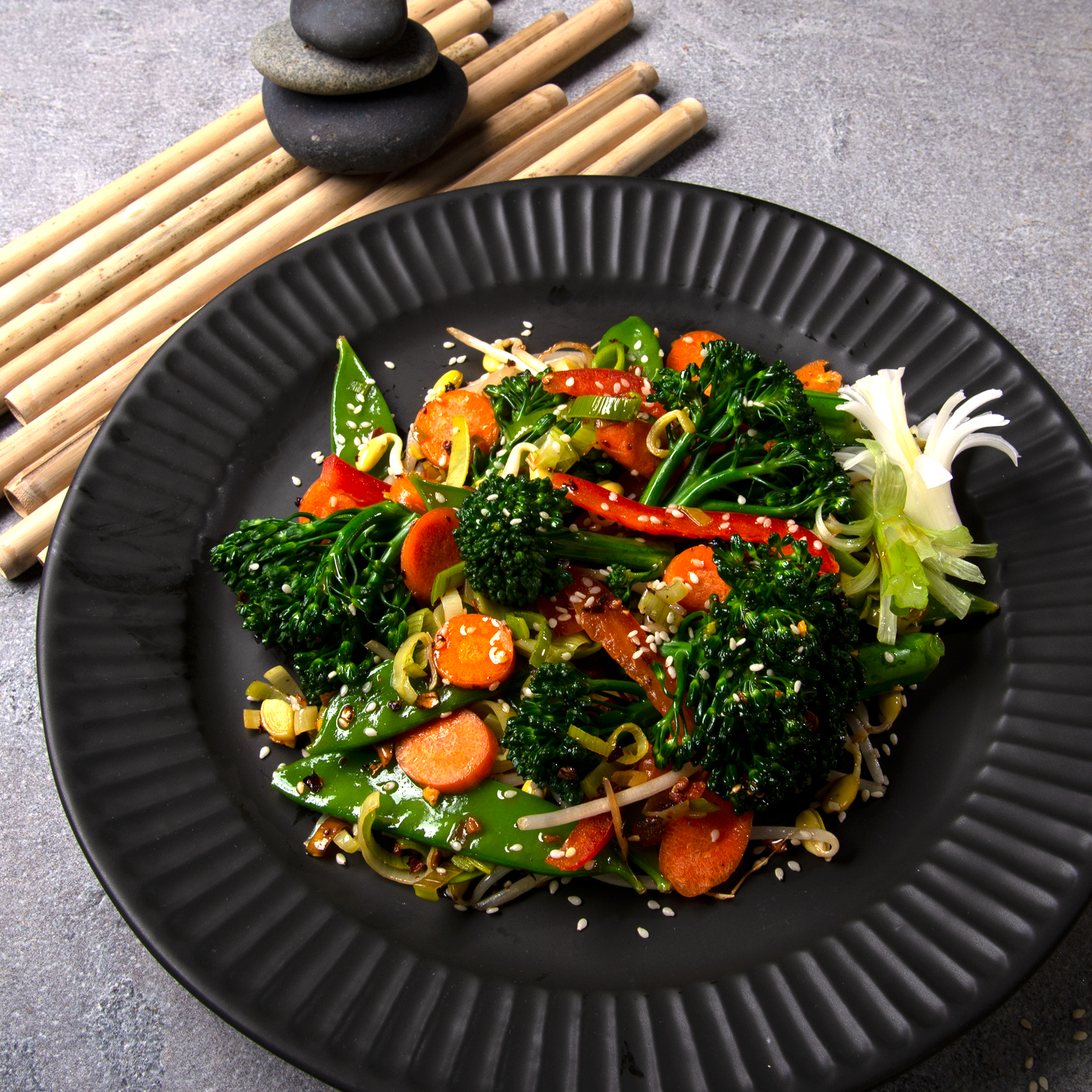 Black plate with veggie stir fry and spicy oo’mämē, broccolini, peppers, carrots, snow peas and bean shoots with hemp hearts #myoomame
